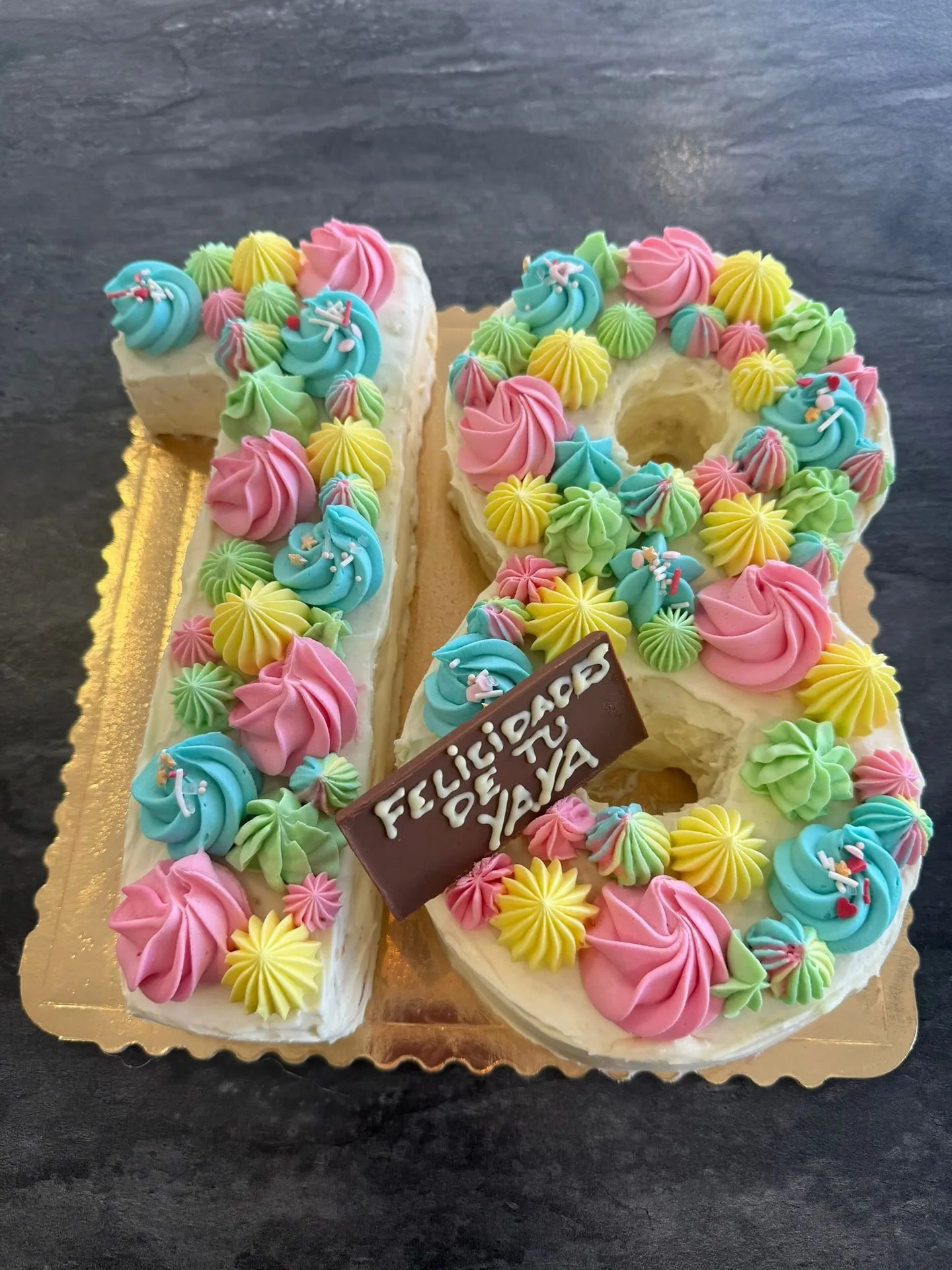 Tarta con forma de 18 cubierta de rosetas de crema de colores y una placa de chocolate