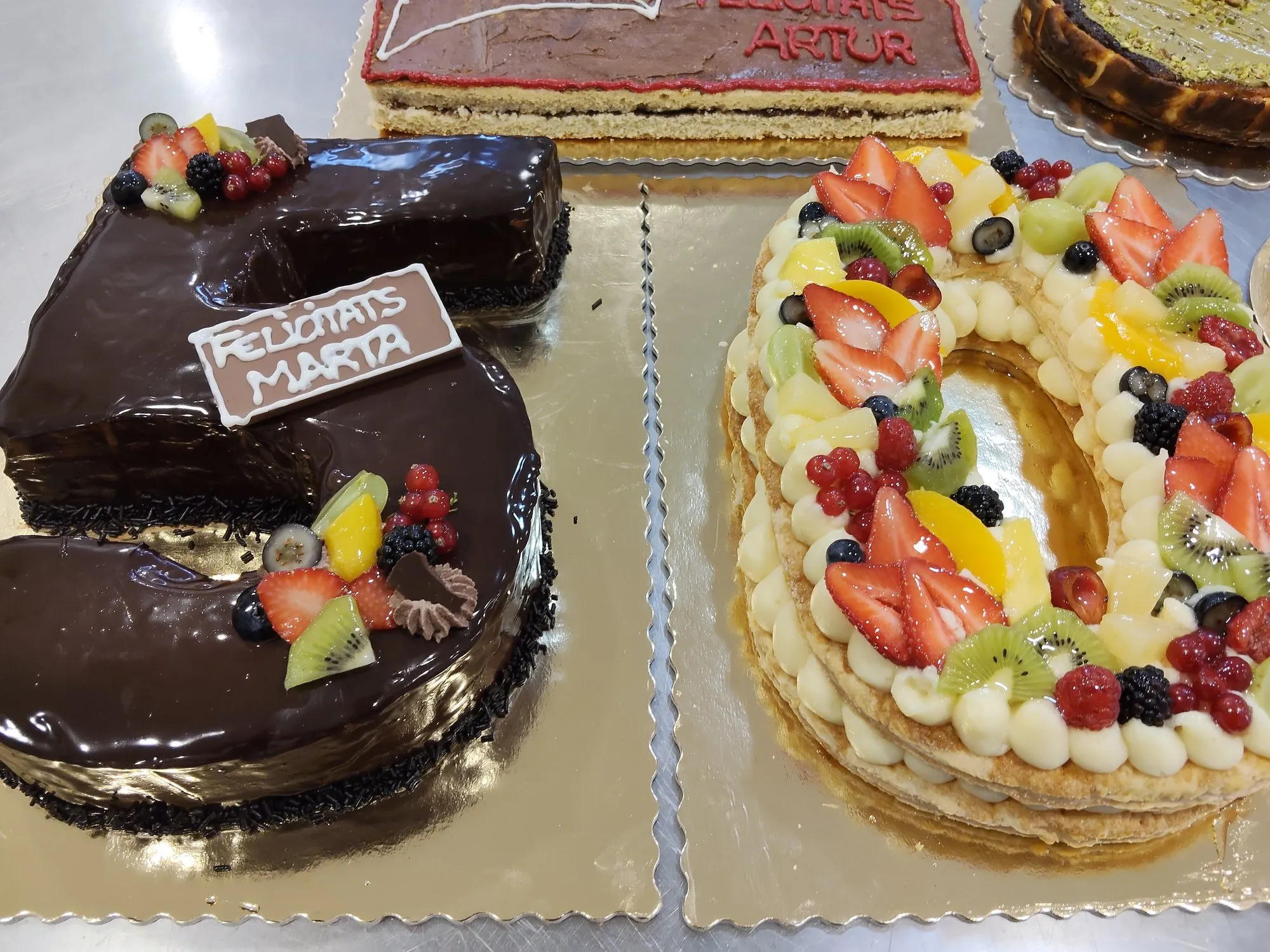 Tartas de números con fruta fresca y una de chocolate con la placa «Felicitats Marta»